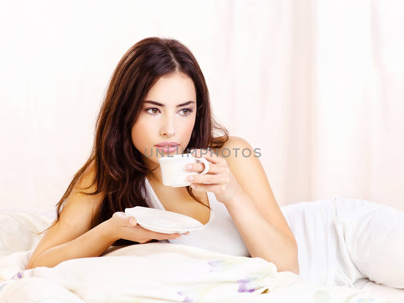 Pretty woman white dressed dink coffee in bed