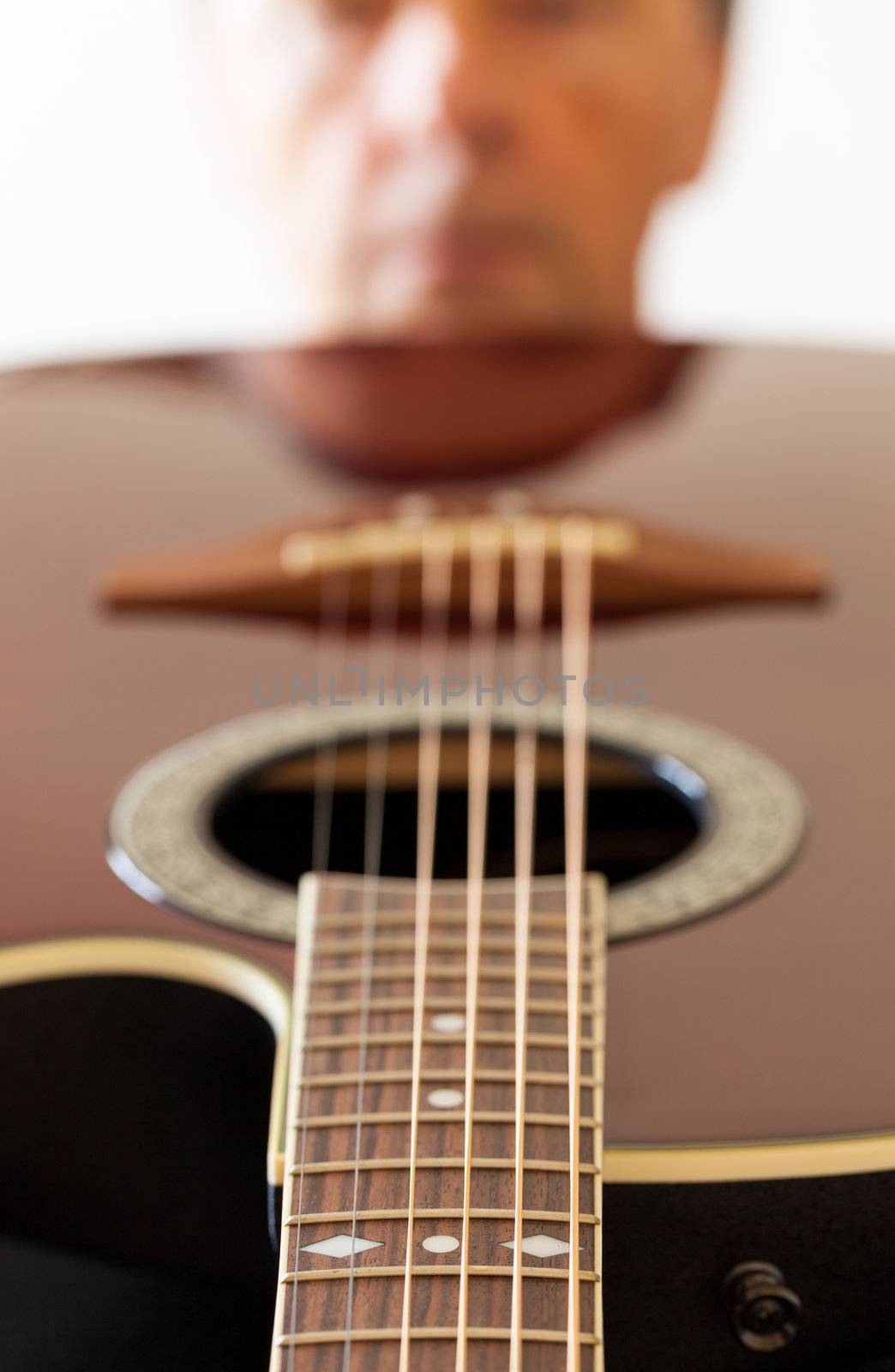 Macro shot down the fretboard of acoustic guitar with shallow depth of field with guitarist face in the distance reflected