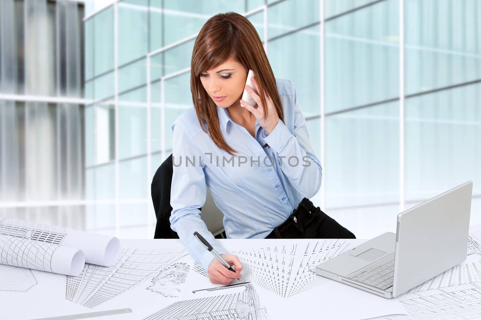 Attractive young female architect working at desk with plans.