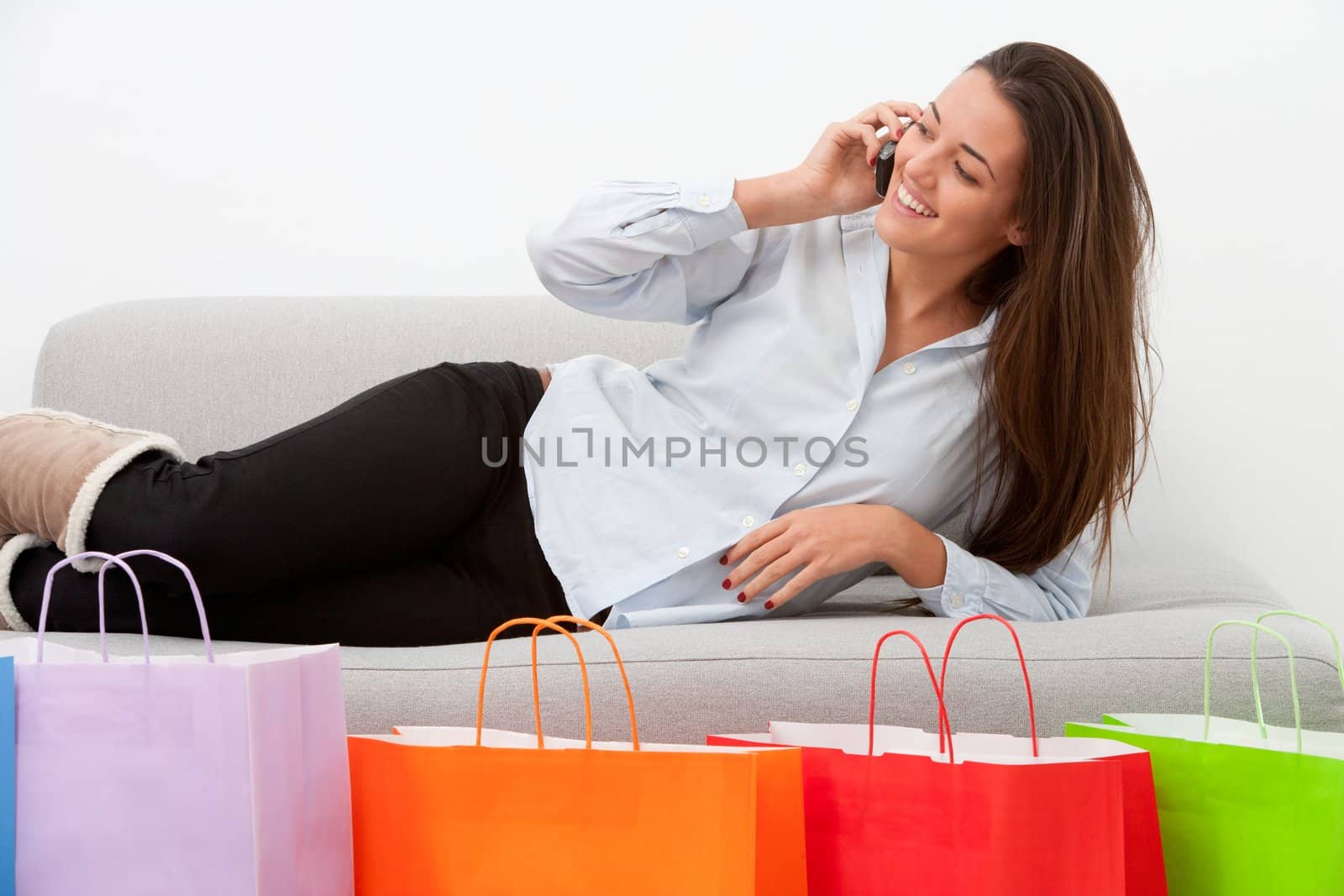 Girl on couch with mobile and shopping bags by karelnoppe
