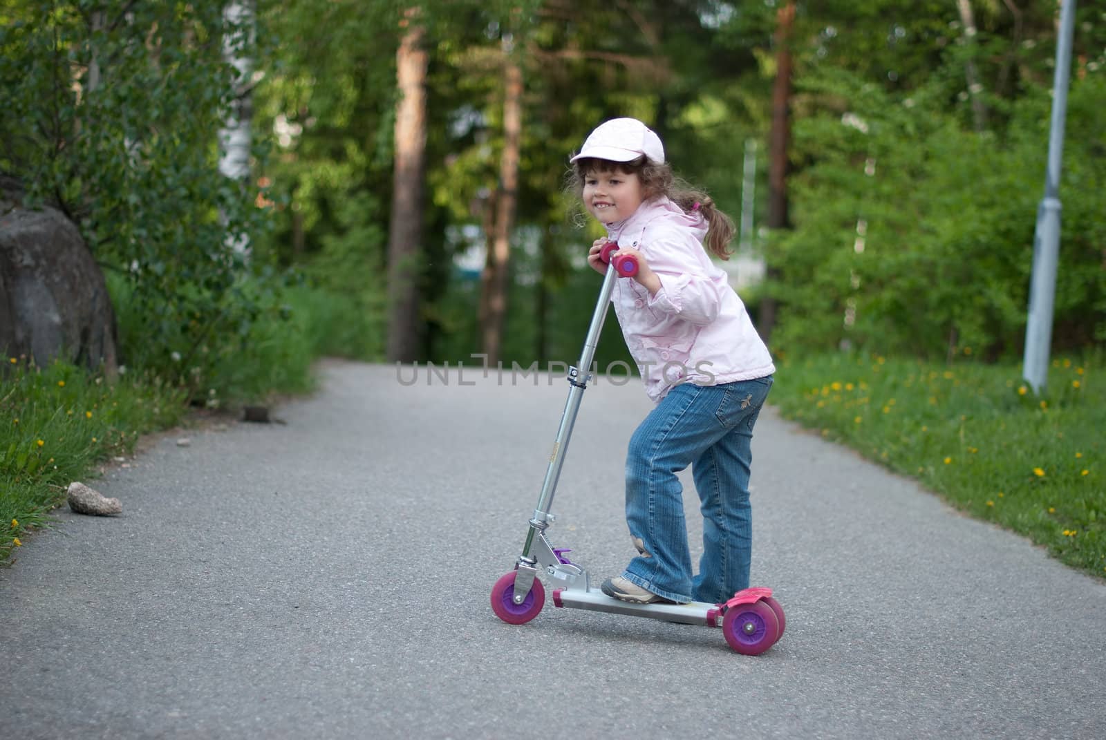 A girl riding a scooter in the park.