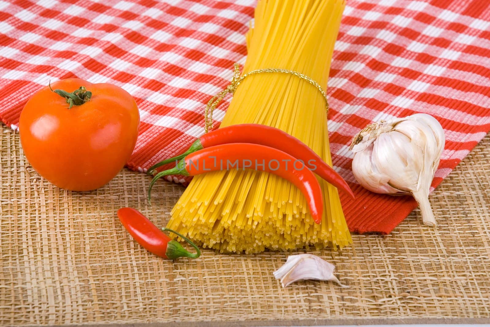 Golden raw dried Italian pasta with other ingredients on kitchen desk.