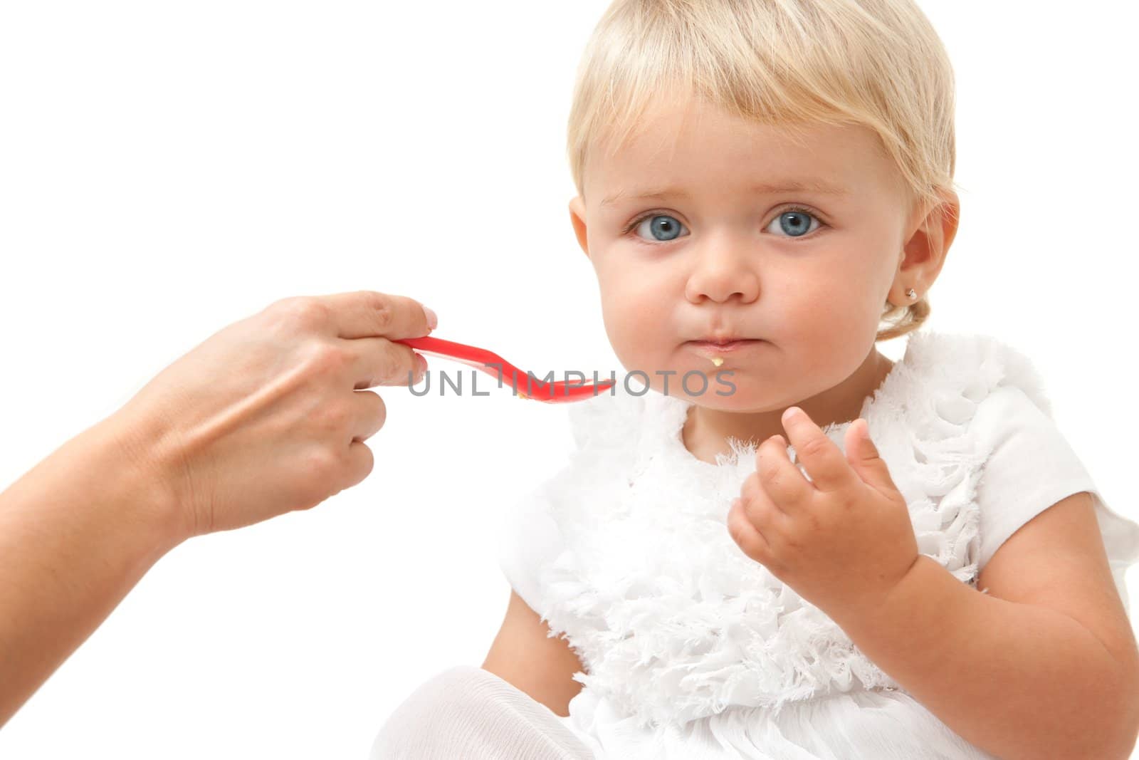 Portrait of blue eye baby girl being fed by hand with red spoon.Isolated on white background.