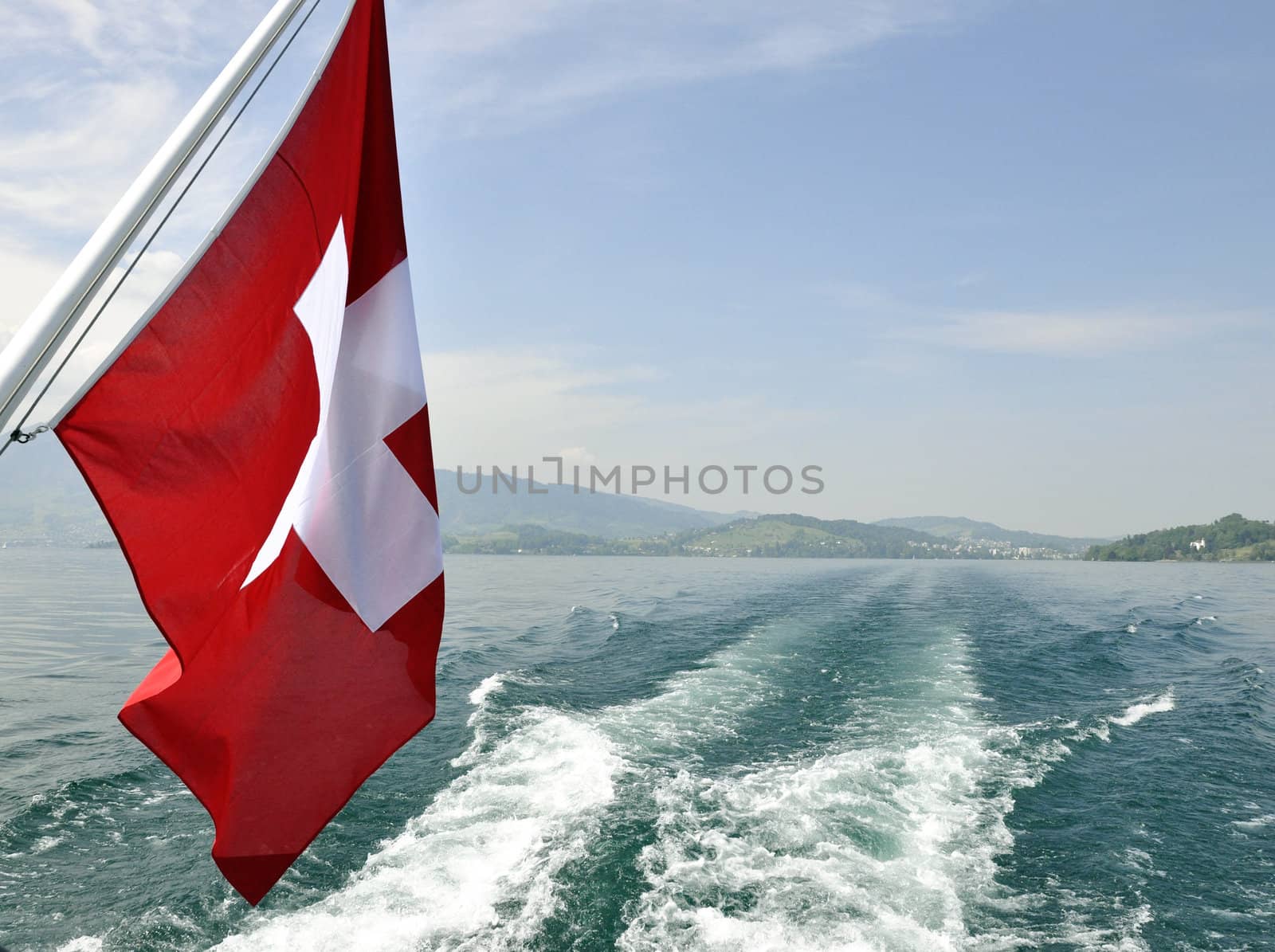 Swiss flag in boat, during summer. Lake and mountains in the back.