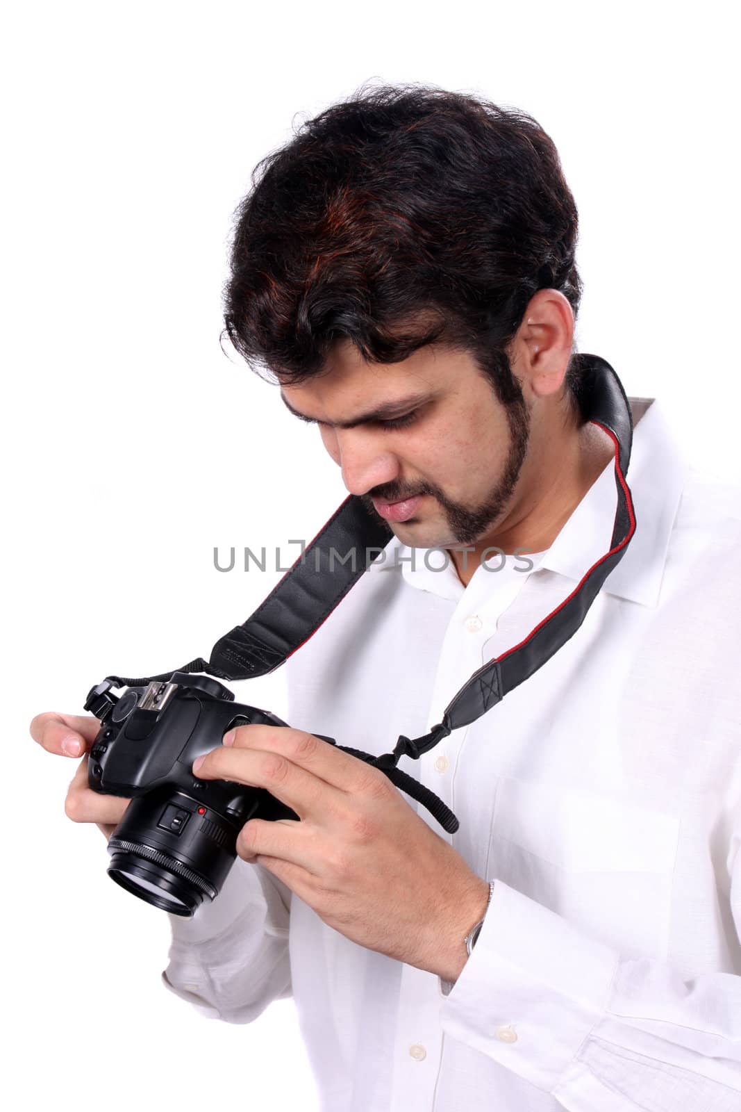 A young Indian professional photographer checking the quality of the photographs after clicking them, on white studio background.