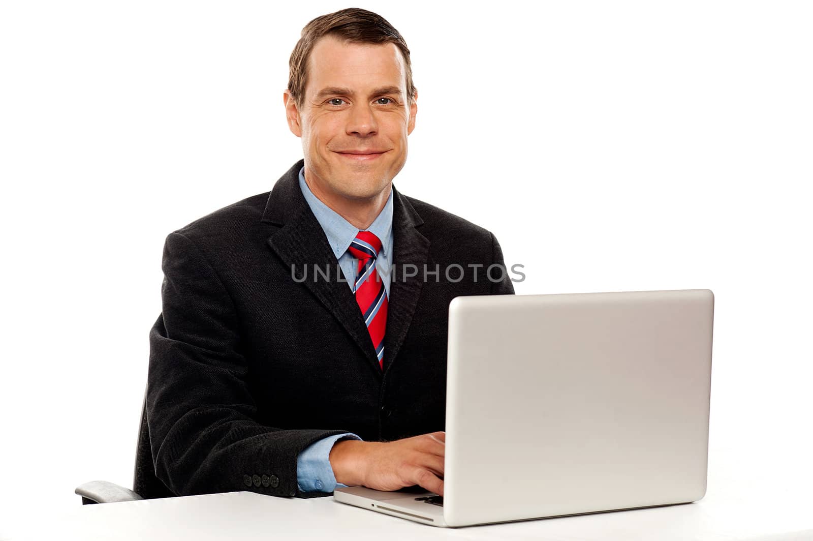 Male executive at work desk operating laptop and smiling camera
