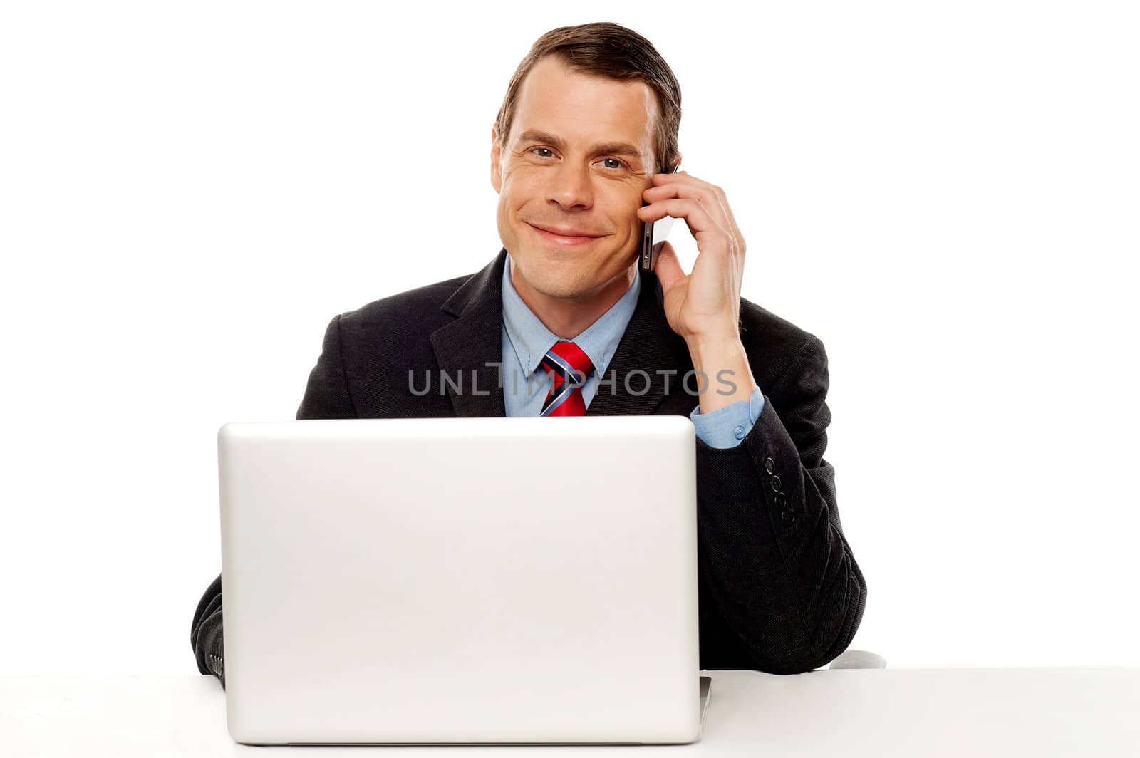 Businessman sitting in front of laptop on work desk and talking on cell phone