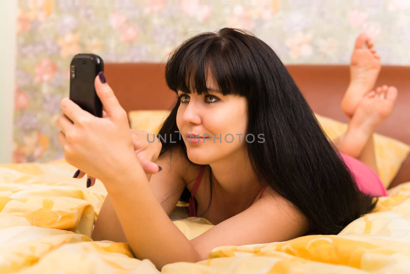 Smiling young woman with a mobile phone in bed