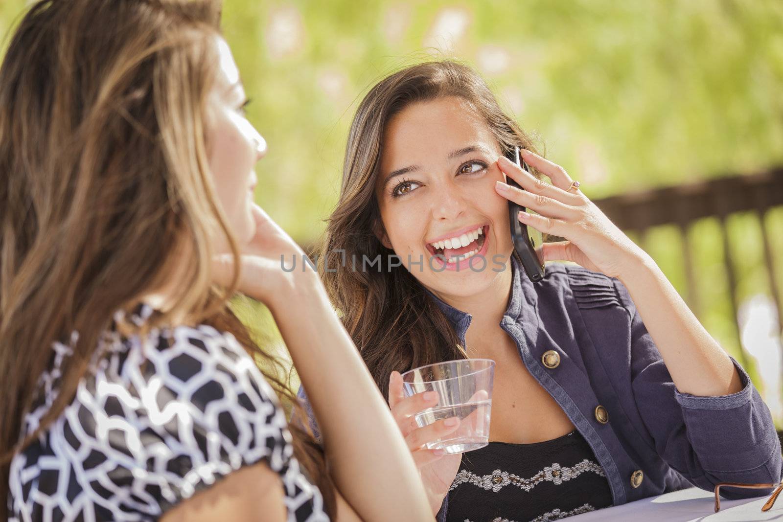 Mixed Race Girls Talking on Thier Mobile Cell Phones Sitting Outside at a Table.