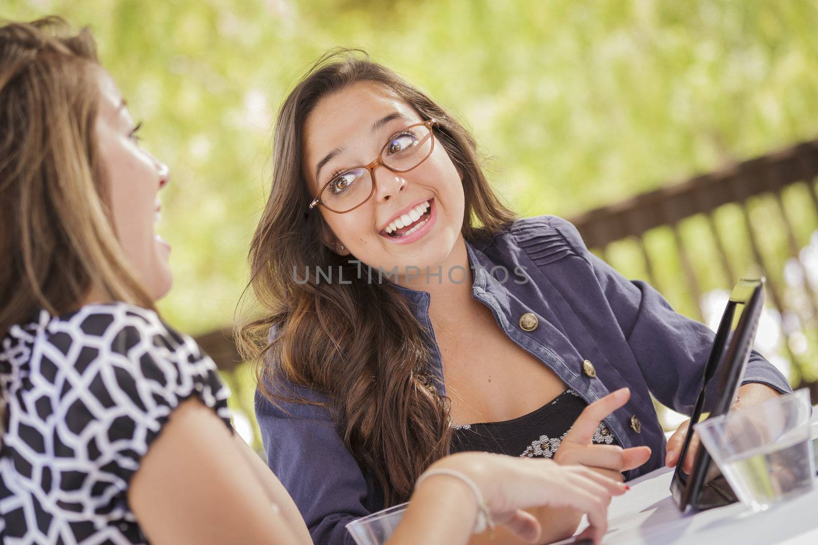 Attractive Mixed Race Girls Smiling and Talking While Working on Tablet Computer Sitting Outdoors.