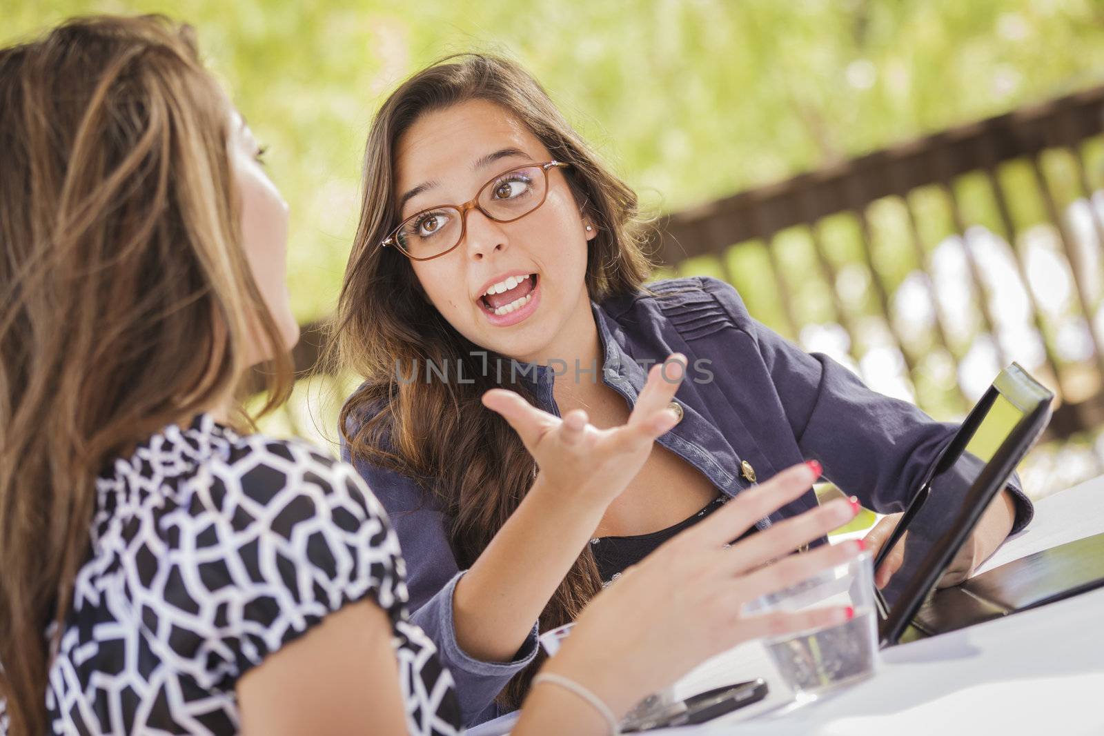 Attractive Mixed Race Girls Smiling and Talking While Working on Tablet Computer Sitting Outdoors.