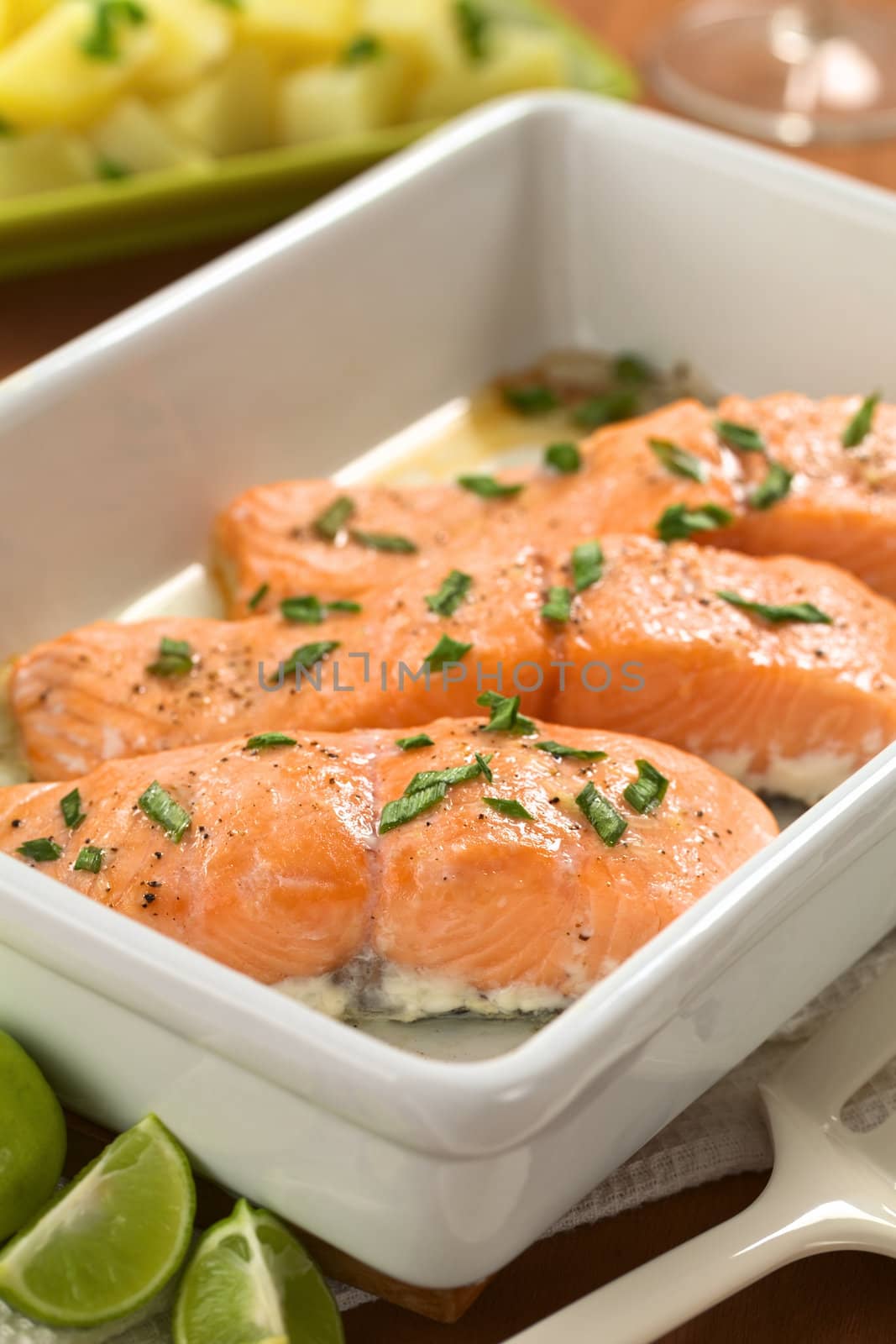Baked salmon with shallots in casserole with lime wedges in the front and boiled potatoes in the back (Selective Focus, Focus on the front edge of the first salmon piece) 