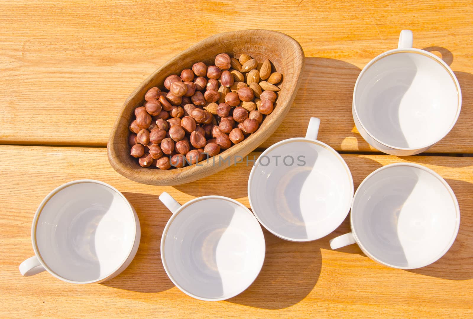 Hazelnuts packed in wooden dish and cups placed on table outside illuminate sun and shadows.