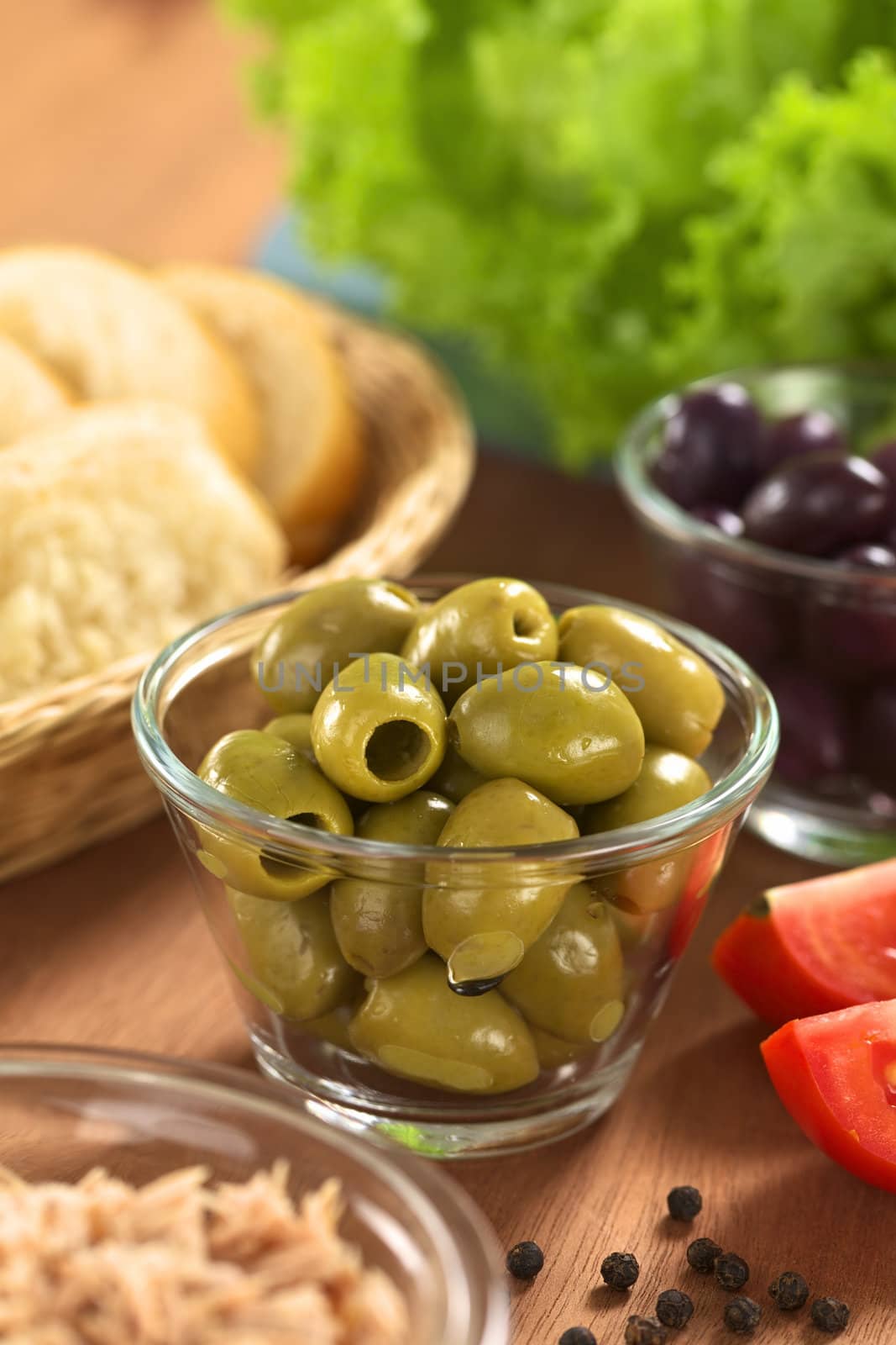 Preparing a fresh salad. Green olives with tuna, tomatoes, black olives, lettuce and bread (Selective Focus, Focus on the green olives on the top) 