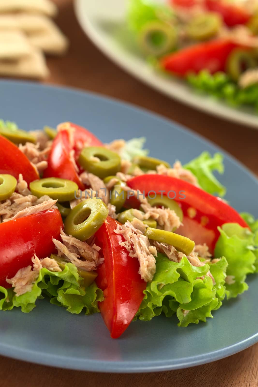 Fresh tuna, tomato and green olive salad served on lettuce leaf on blue plate (Selective Focus, Focus on the front of the olive in the middle of the salad) 