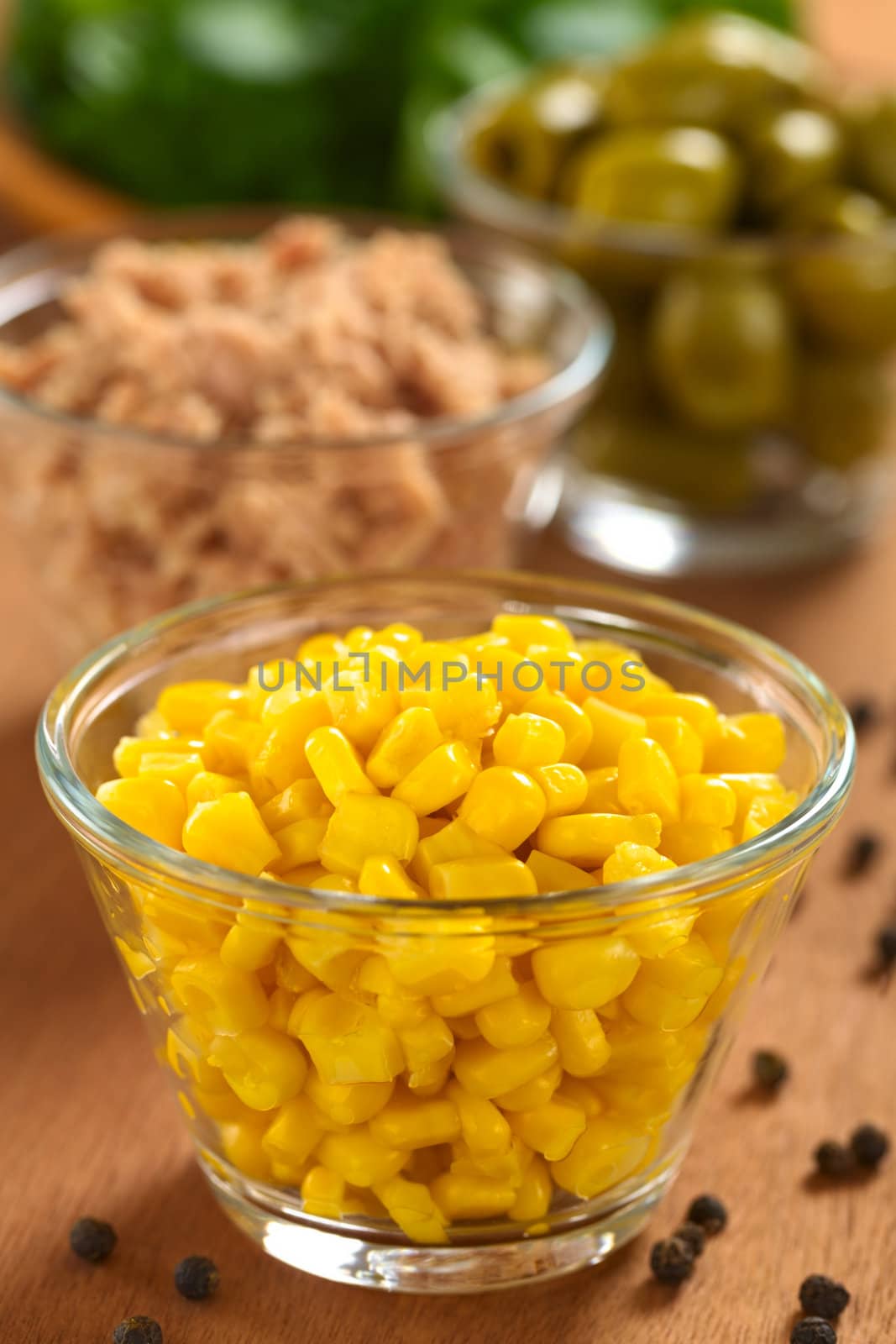 Preparing a salad. Sweet corn grains in glass bowl with other ingredients (tuna, green olives and watercress) in the back (Selective Focus, Focus one third into the corn)