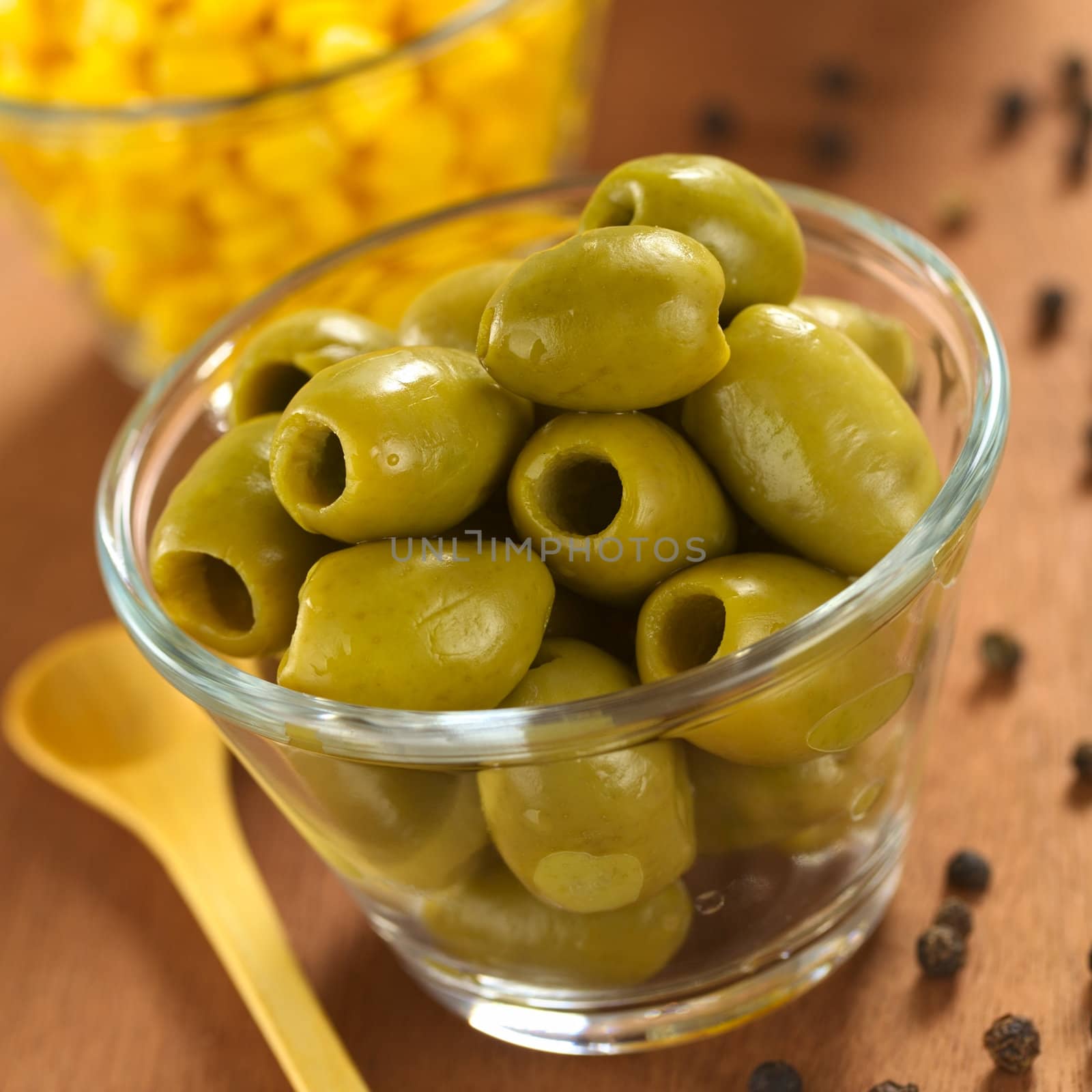 Green olives and sweet corn in glass bowls with black pepper corns on the side (Selective Focus, Focus on the front of the olives on the top) 
