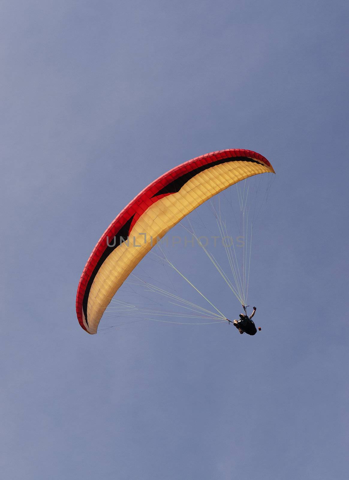 Red, yellow and black para glider against a blue sky.