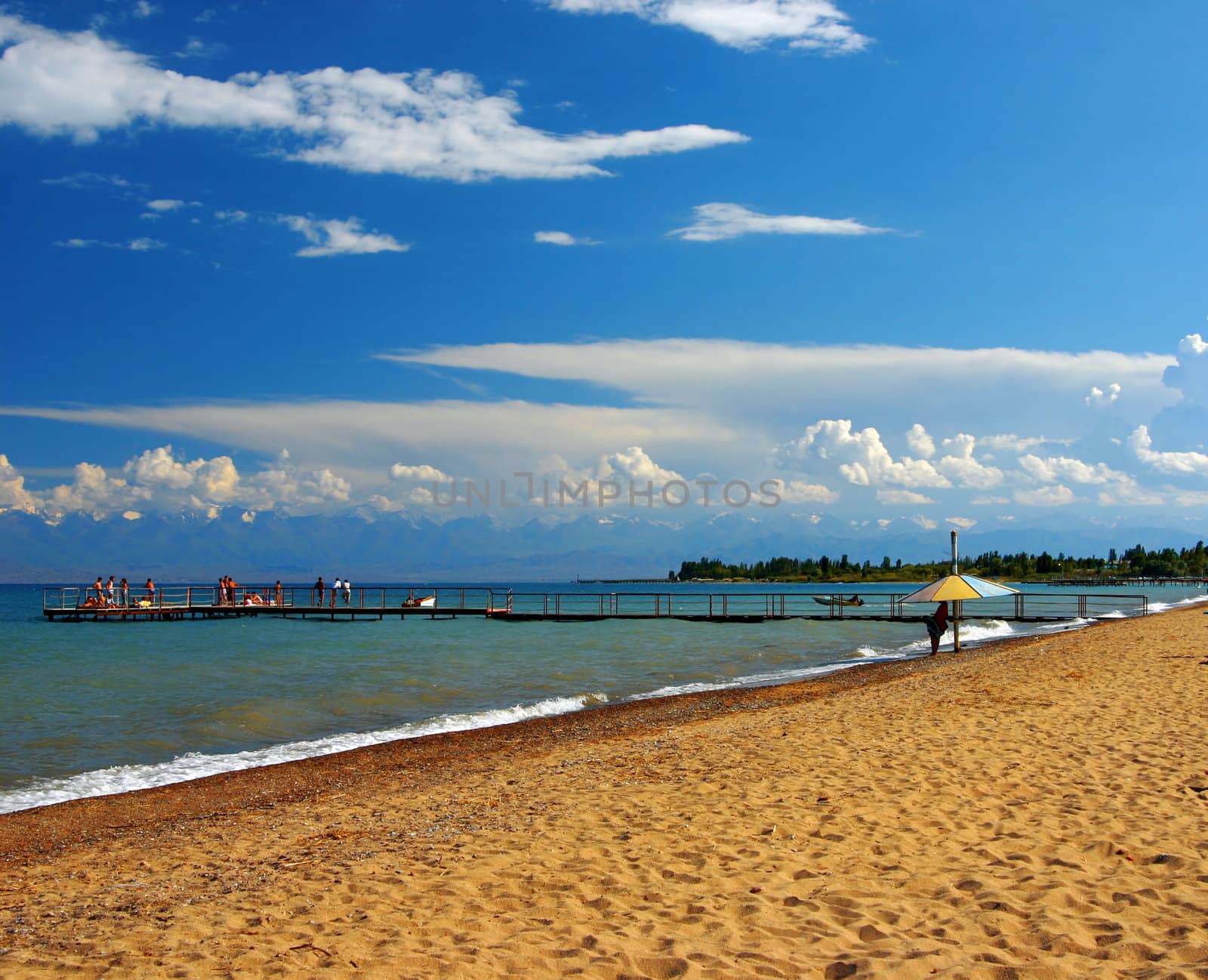 Sandy beach with a pier against the blue sky of the sea and far mountains