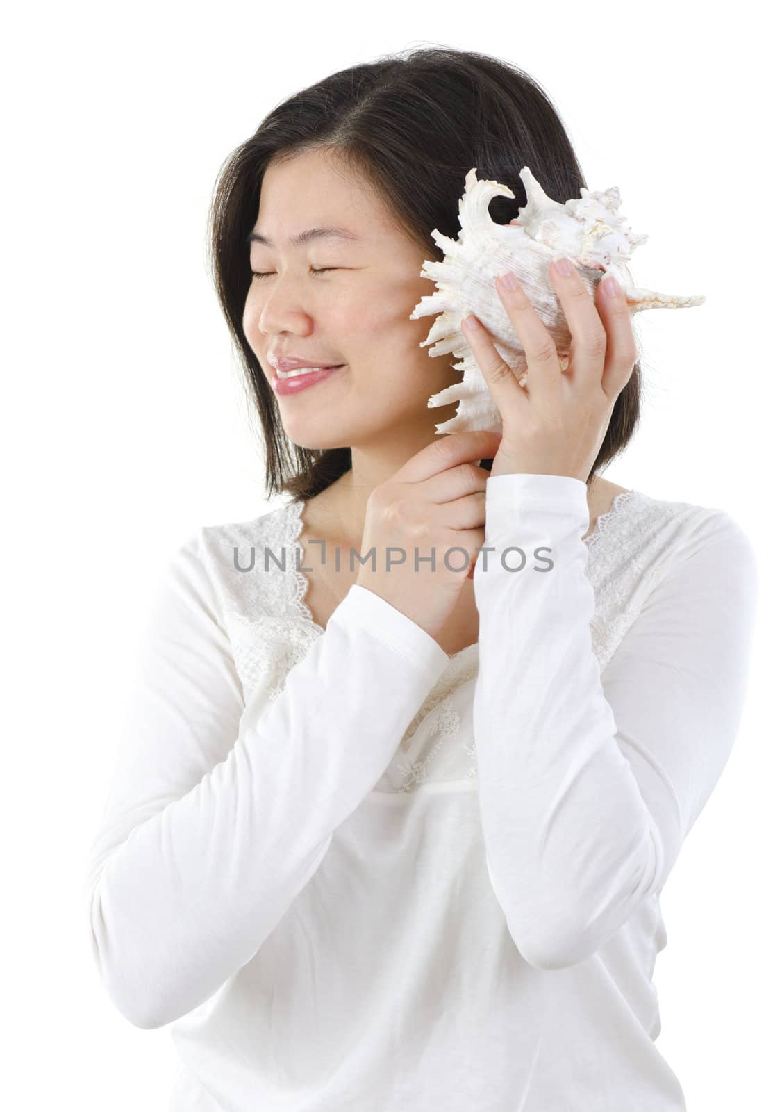 Asian female listening to a seashell over white background