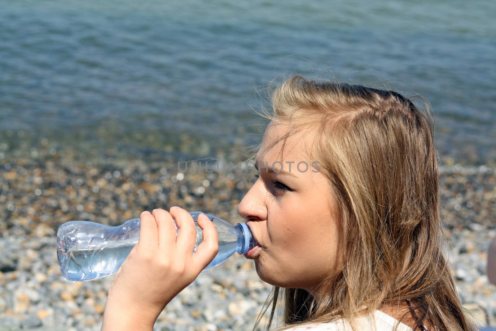 teenage girl drinking water sat on a beach