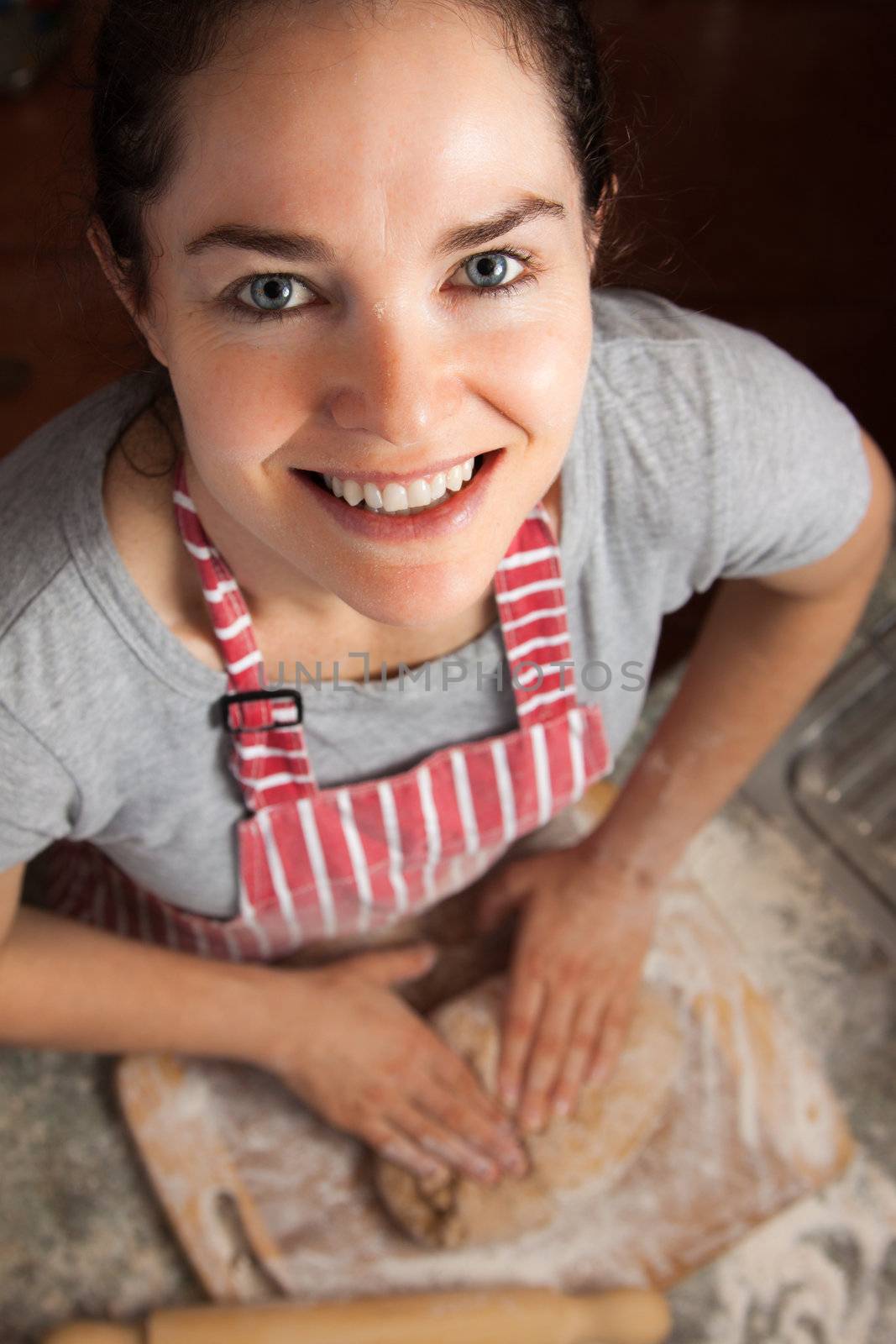 A beautiful middle aged woman kneading a dough and smiling at camera