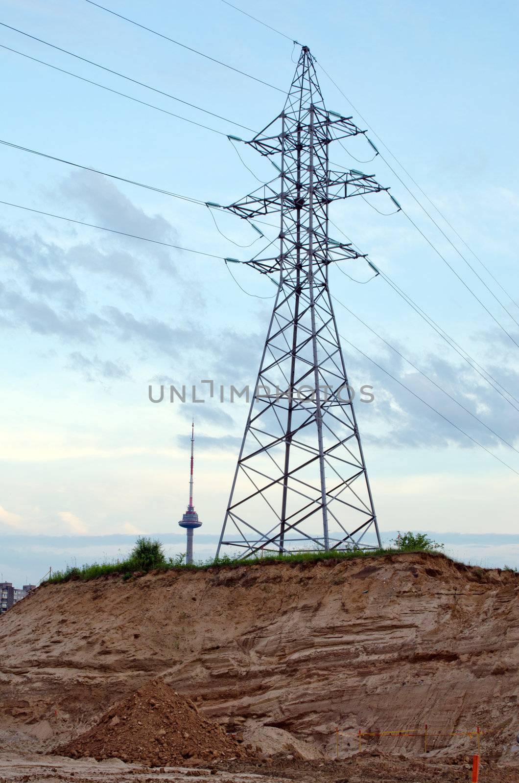 High-voltage power poles and wires on sand hill and television tower in distance.
