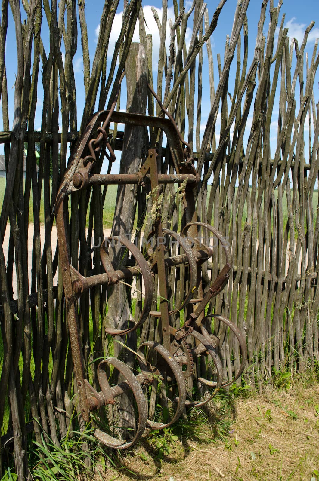 Old corroded field harrow tool stand wooden fence by sauletas