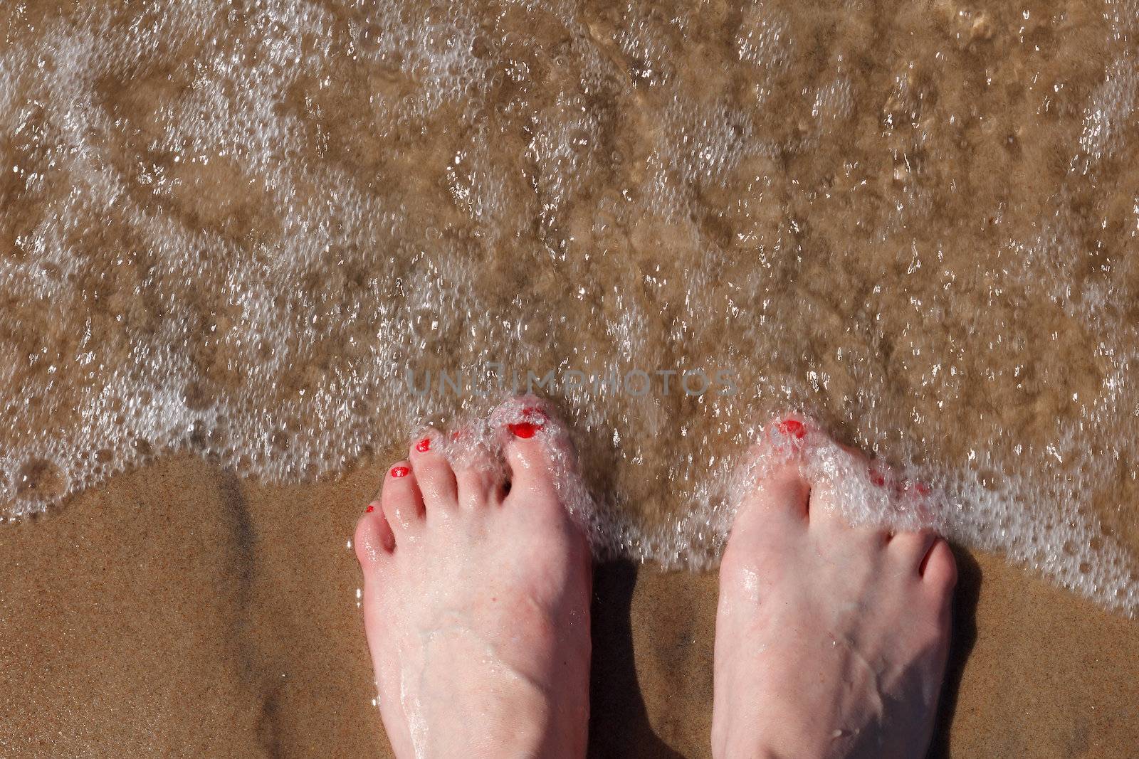 woman's feet in beach sand splashing with sea waves