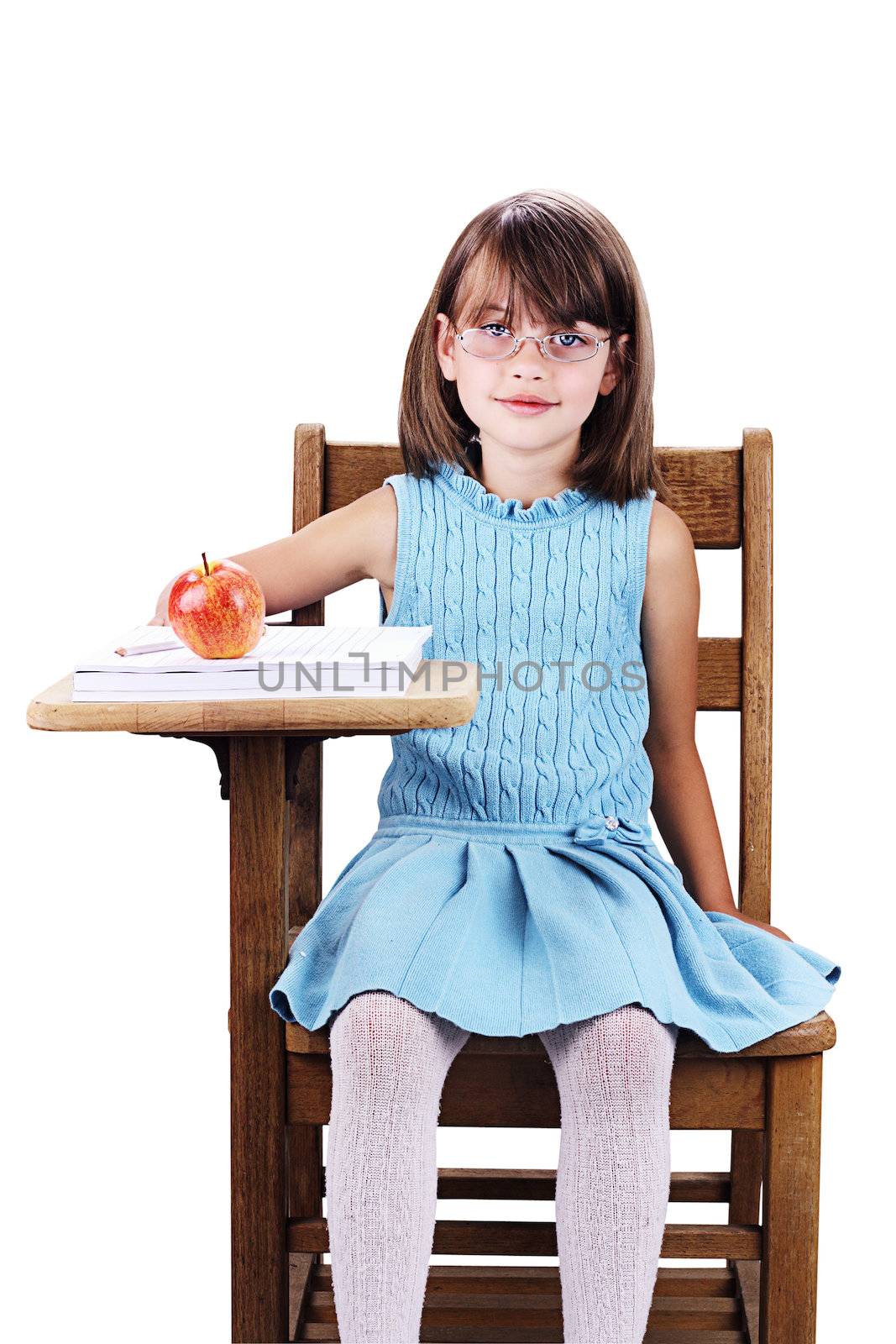Little girl wearing glasses sitting at a school desk with apple and books. Isolated on a white background with clipping path included.