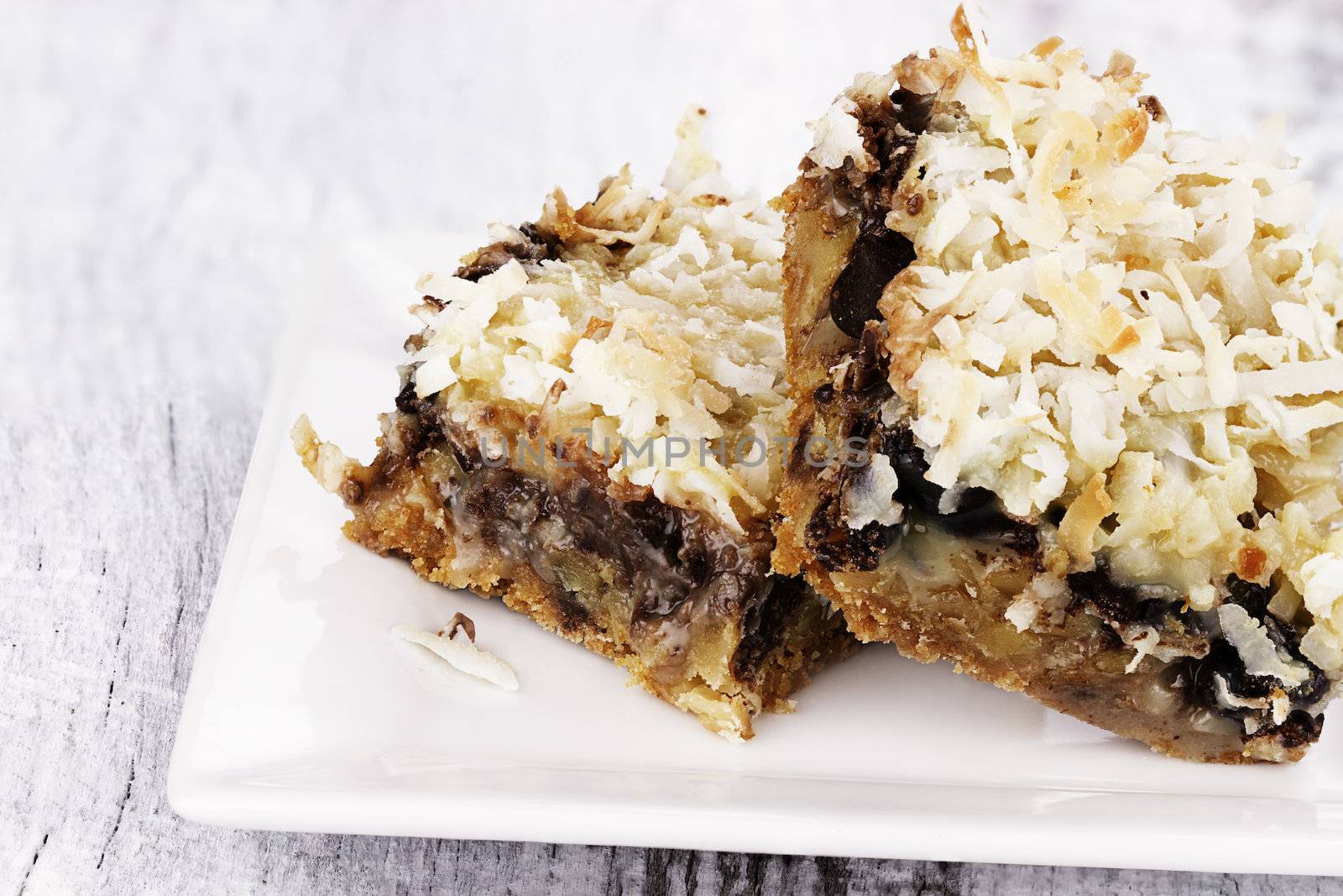 Two coconut chocolate chip bars over a rustic background.