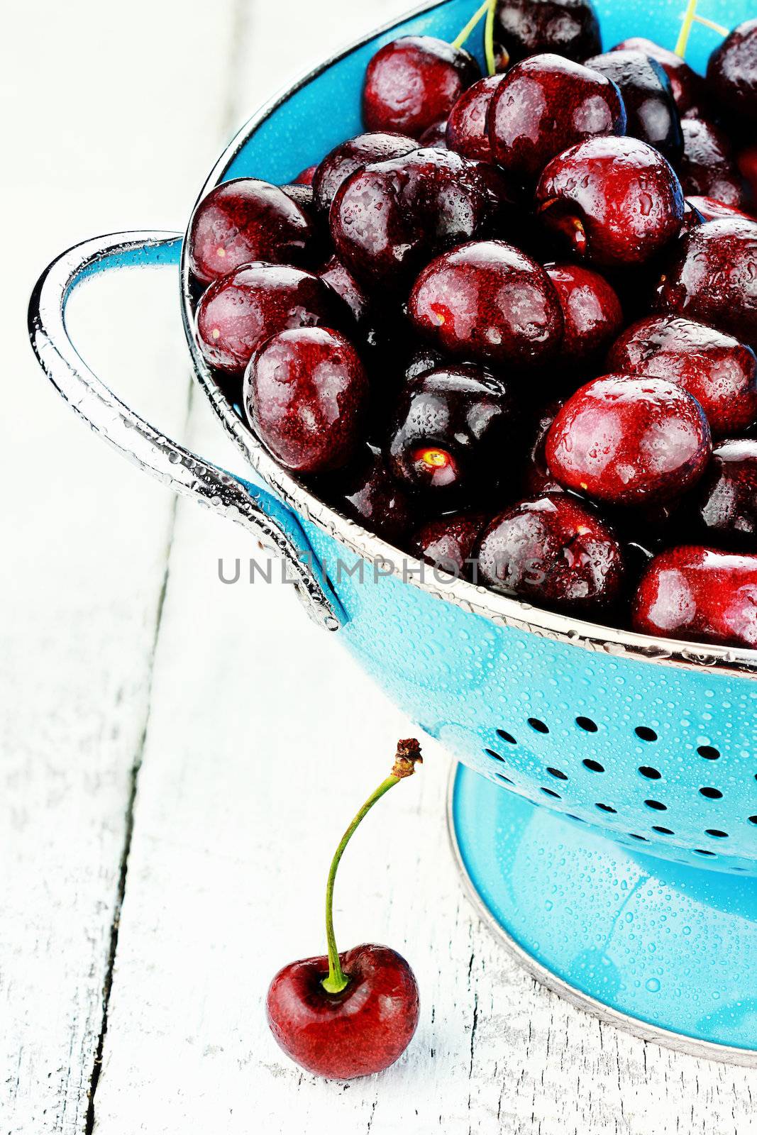 Blue colander filled with fresh black cherries over a rustic background.
