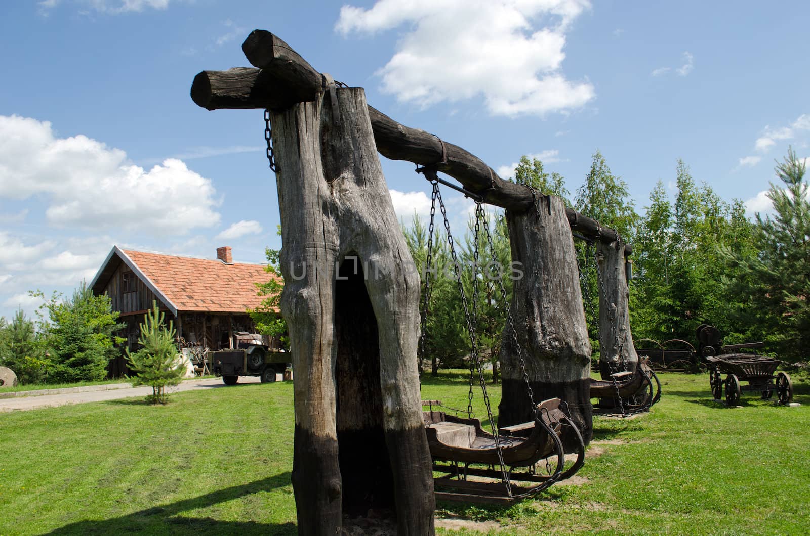 Retro swing made of carriage hang on chains on old tree trunks in park.