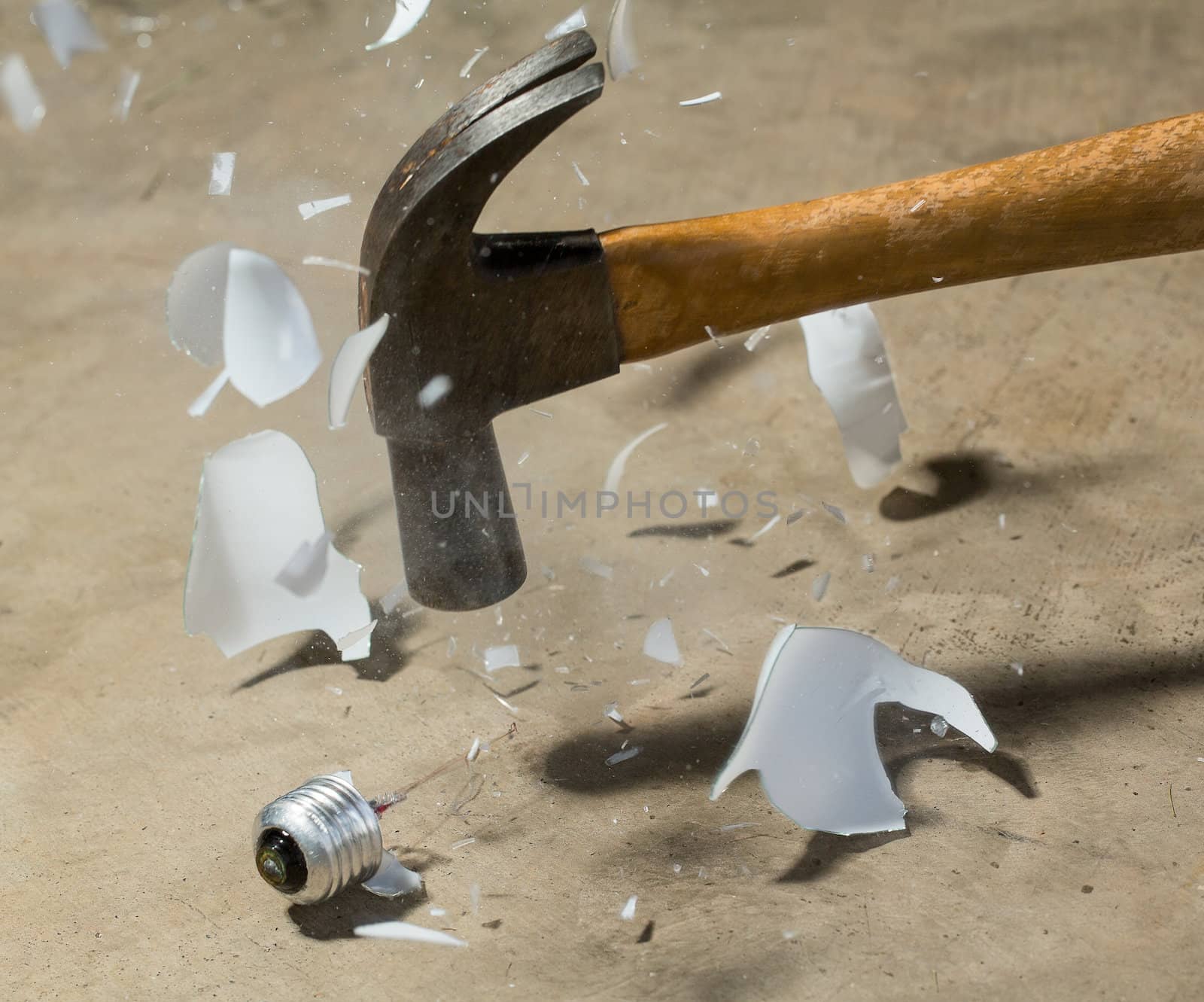 Steel hammer striking glass of incandescent light bulb and smashing it to pieces