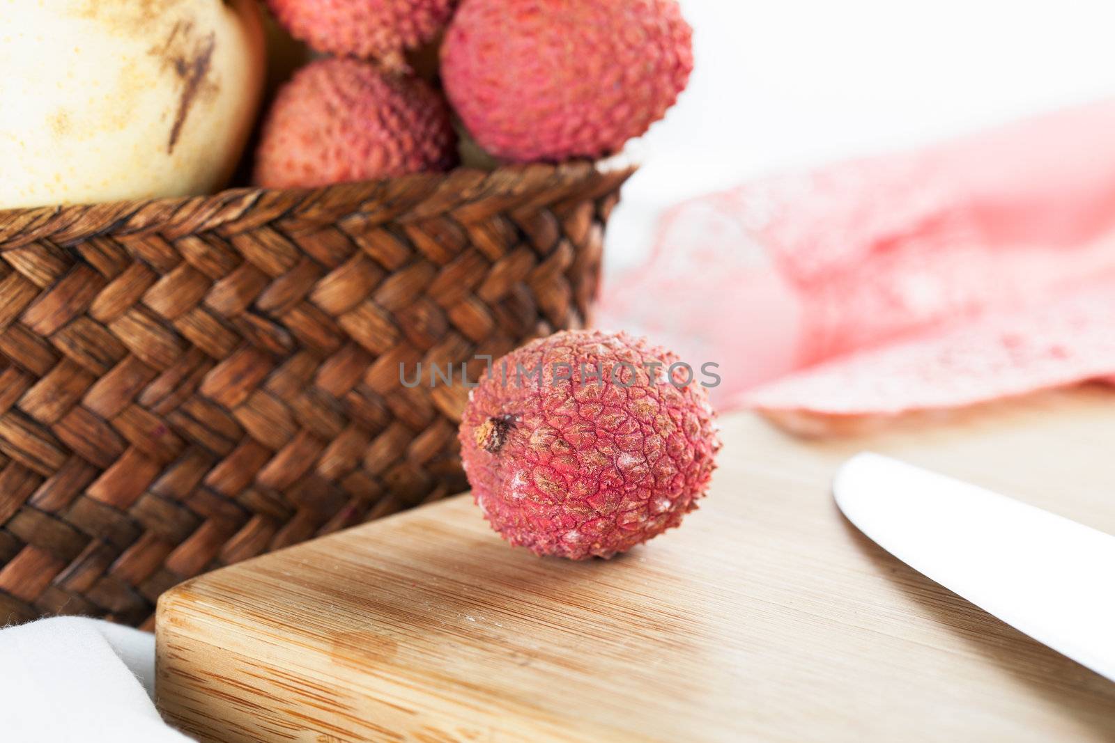 Fresh lychee fruit on cutting board with basket of fruit in background.