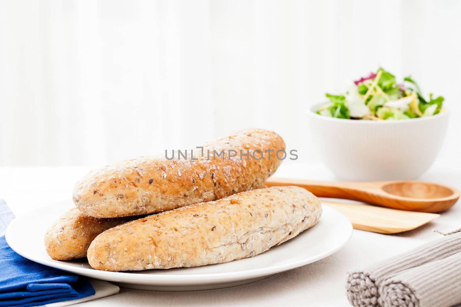 Three bread rolls on the dinner table with salad in the background.