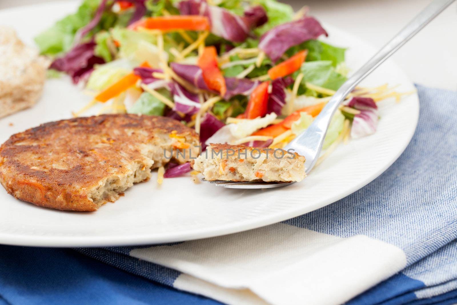 Veggie burger pattie on a plate with a fresh green salad.