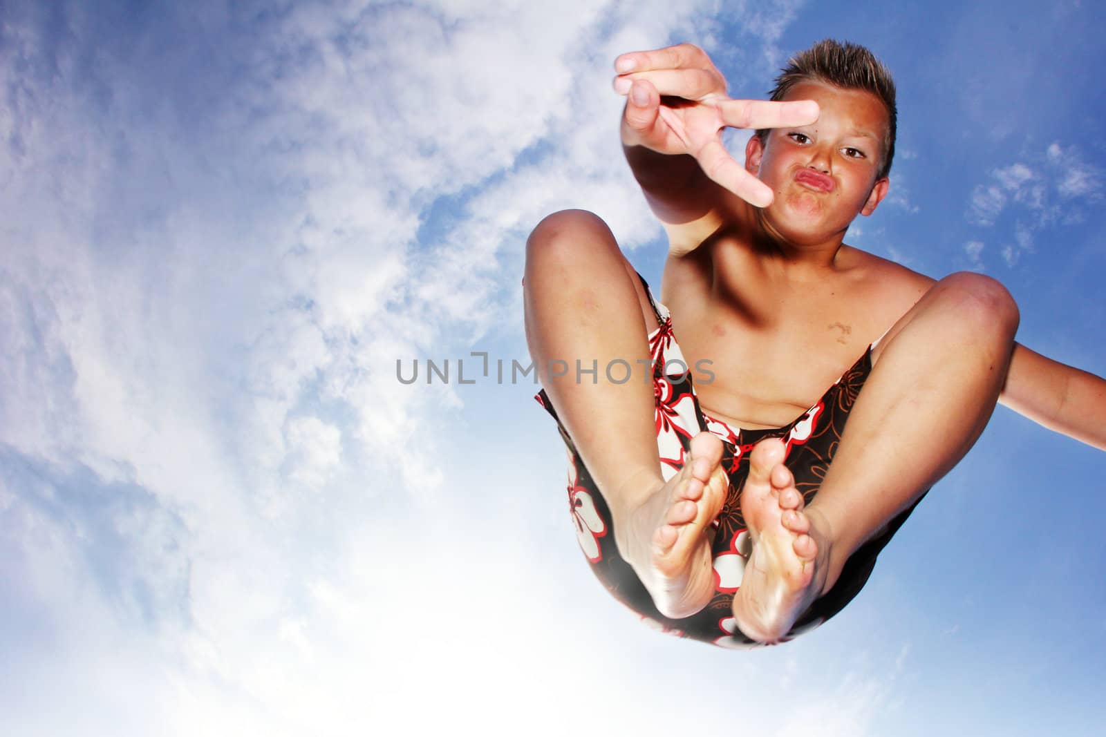 Little boy is jumping in front of the sky showing victory sign