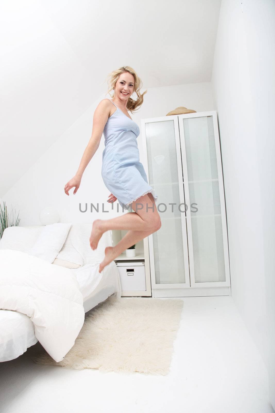 Beautiful blonde healthy happy woman jumping for joy in her lingerie in a modern white bedroom interior 