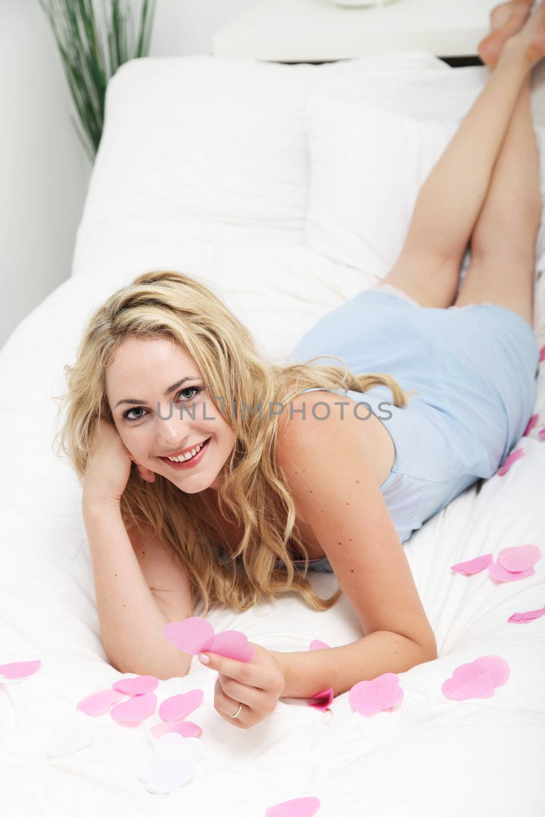 High angle view of a happy romantic young woman lying on her bed sorting pink hearts for Valentine, an anniversary or engagement 