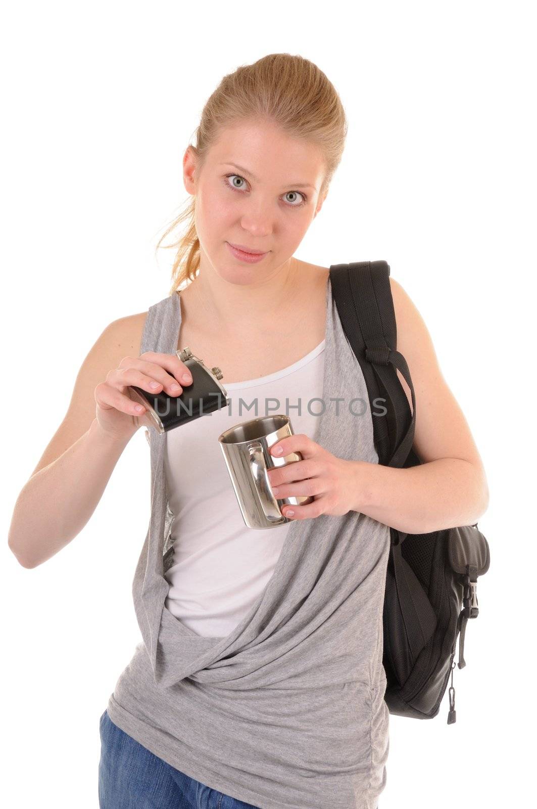 Beauty blonde girl with rucksack is pouring a metal cup from flask on white background