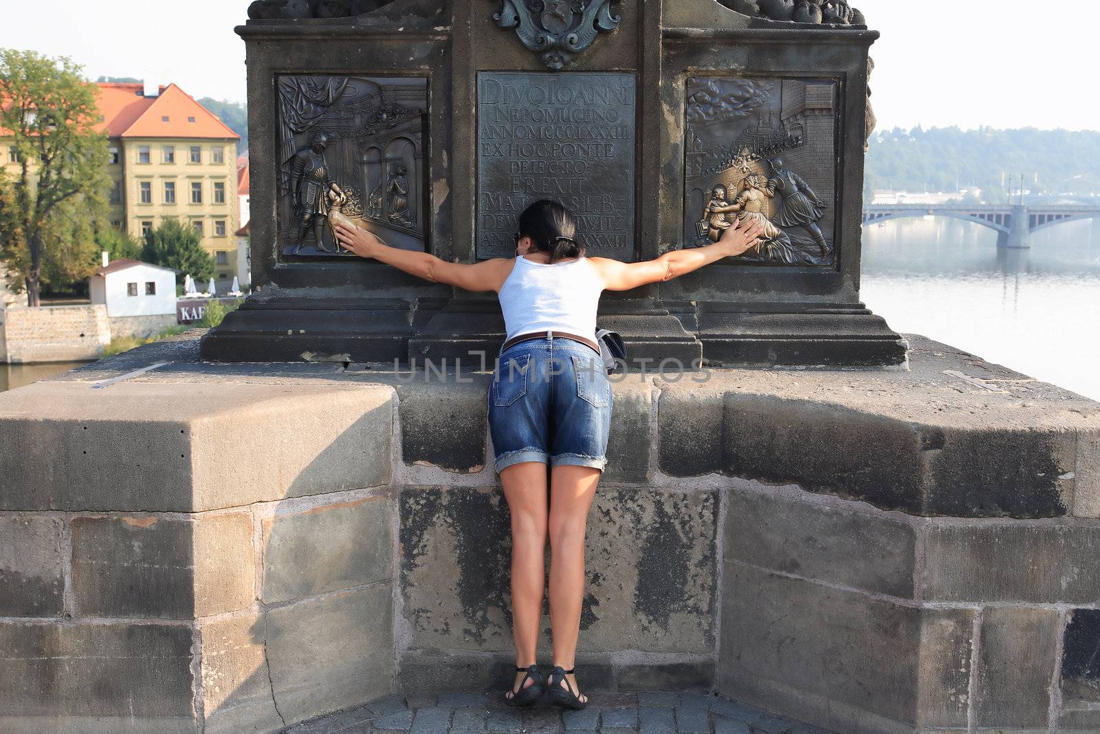 Woman touching ancient sculpture for her wishes. Charles Bridge, Prague,Czech Republic