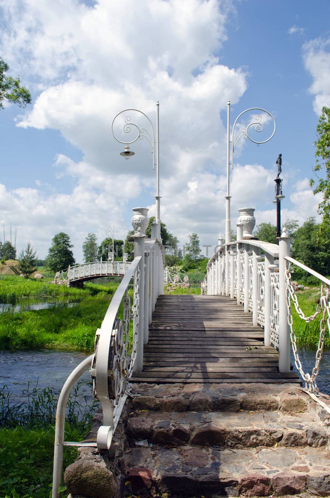 White decorative bridges through park stream and cloudy blue sky.