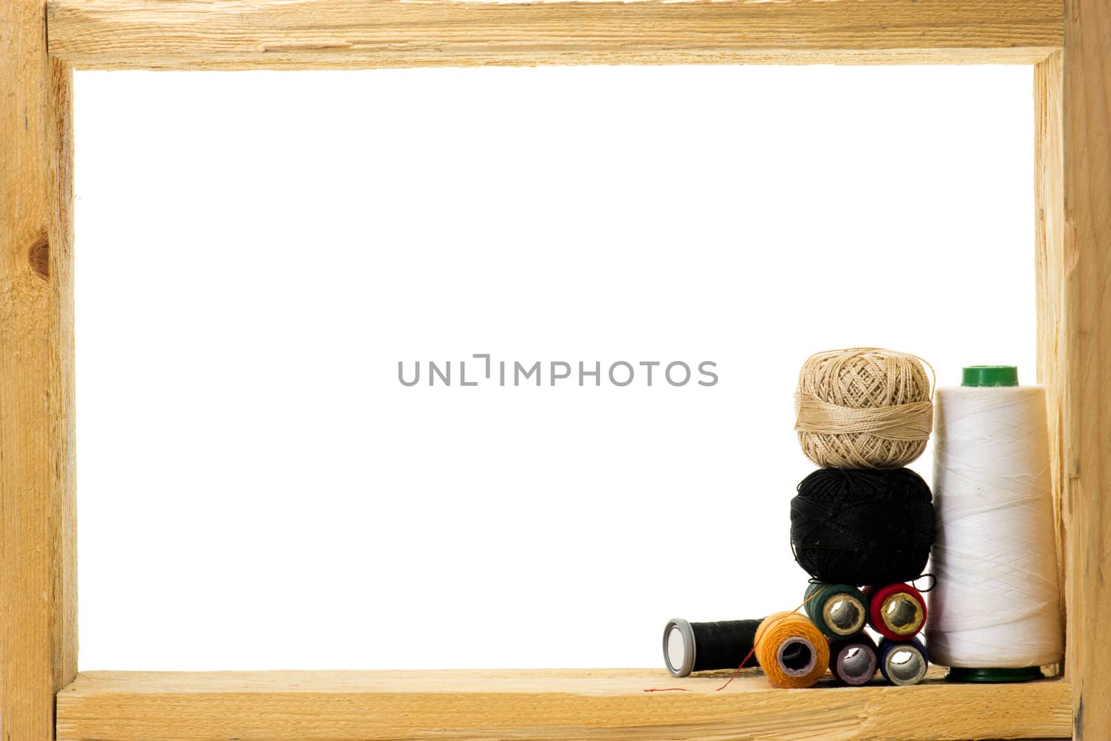 Spools with colored sewing thread inside rough wooden frame on white background 