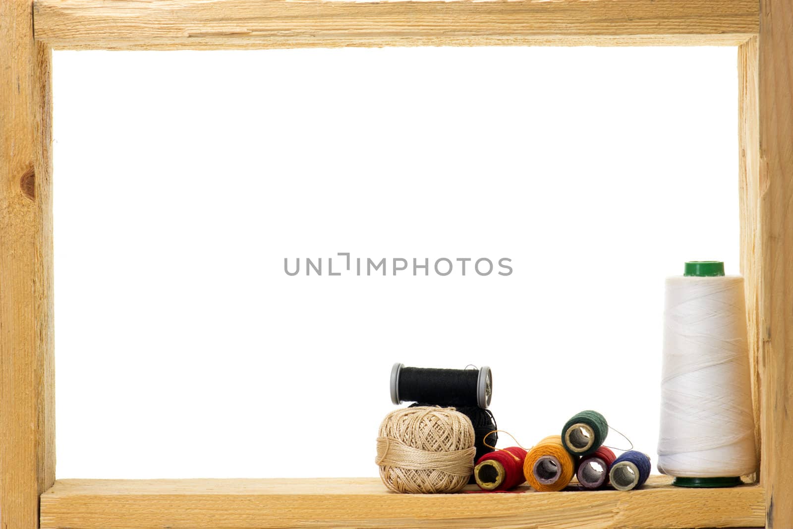 Spools with colored sewing thread inside rough wooden frame on white background 