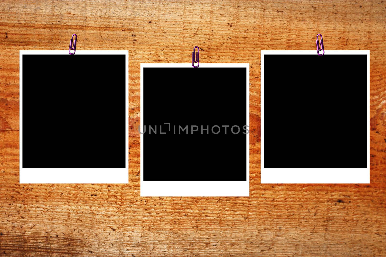 set of three old blank polaroids frames lying on a wood surface  by schankz