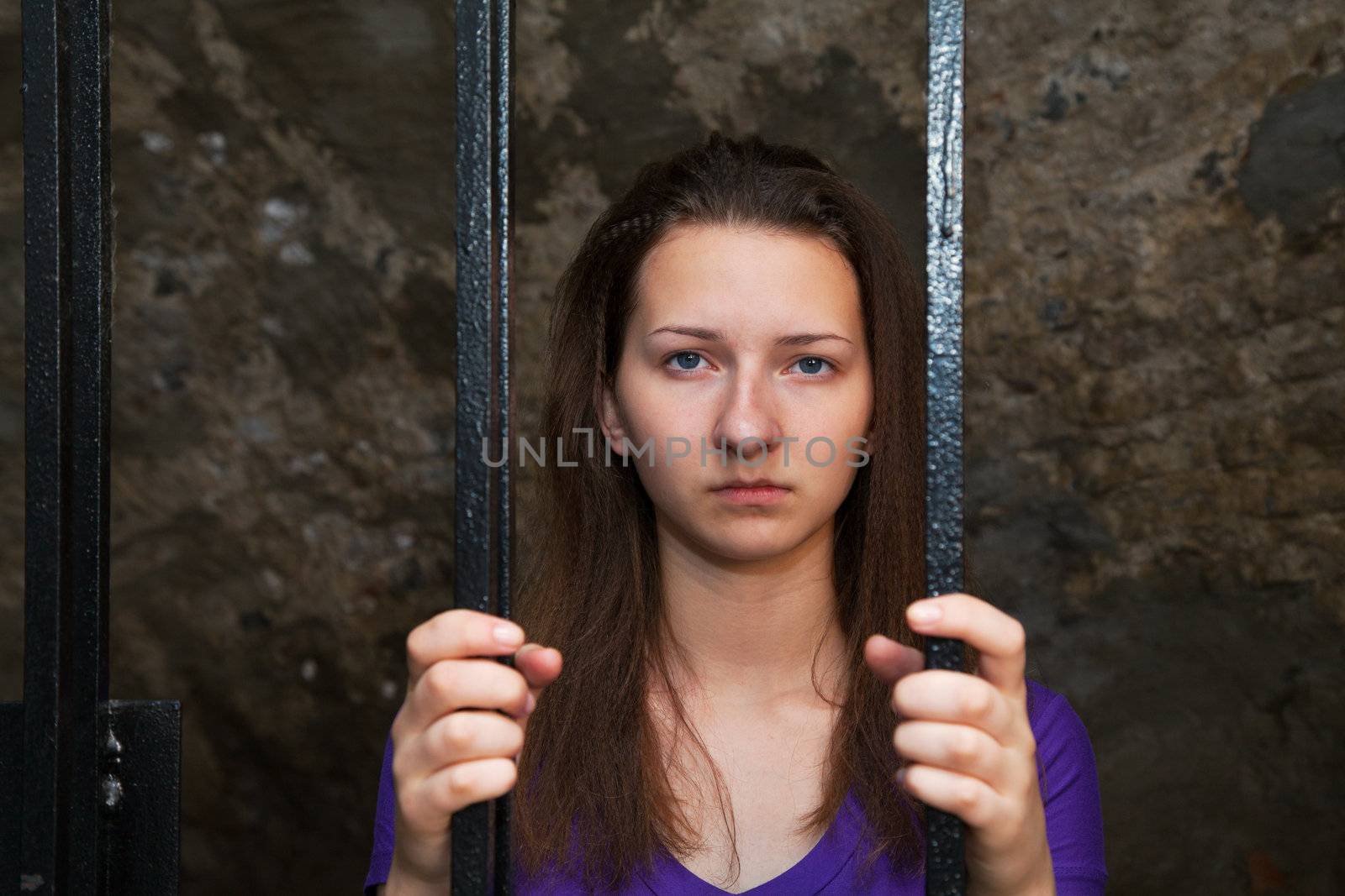 Young woman looking from behind the bars