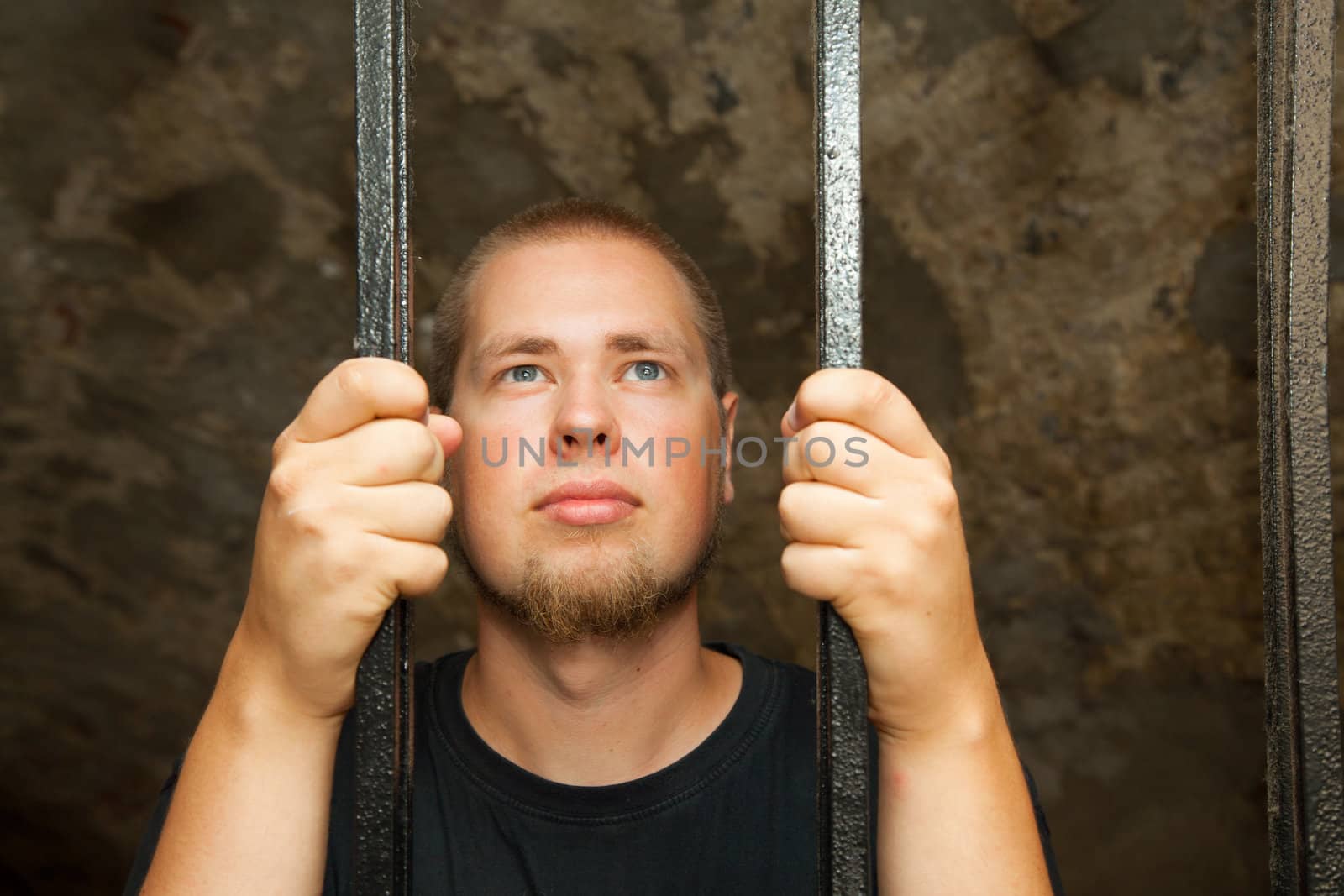 Young man looking from behind the bars
