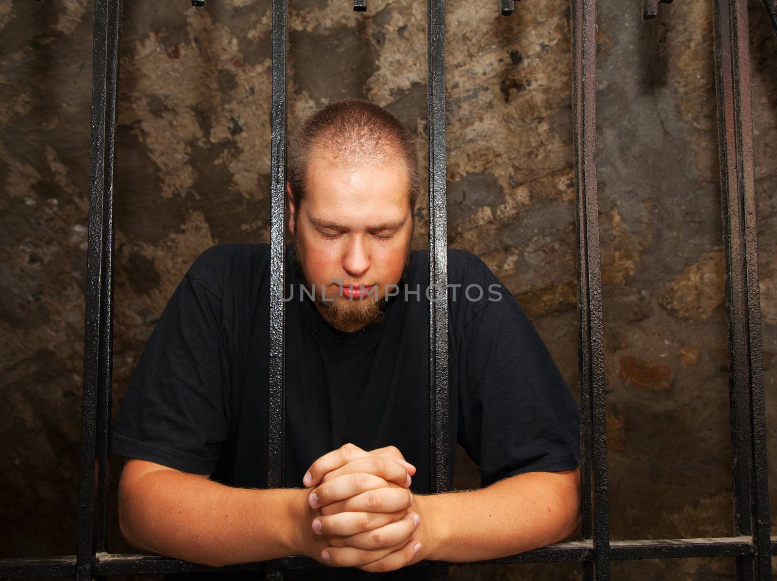 Young man praying staying behind the bars