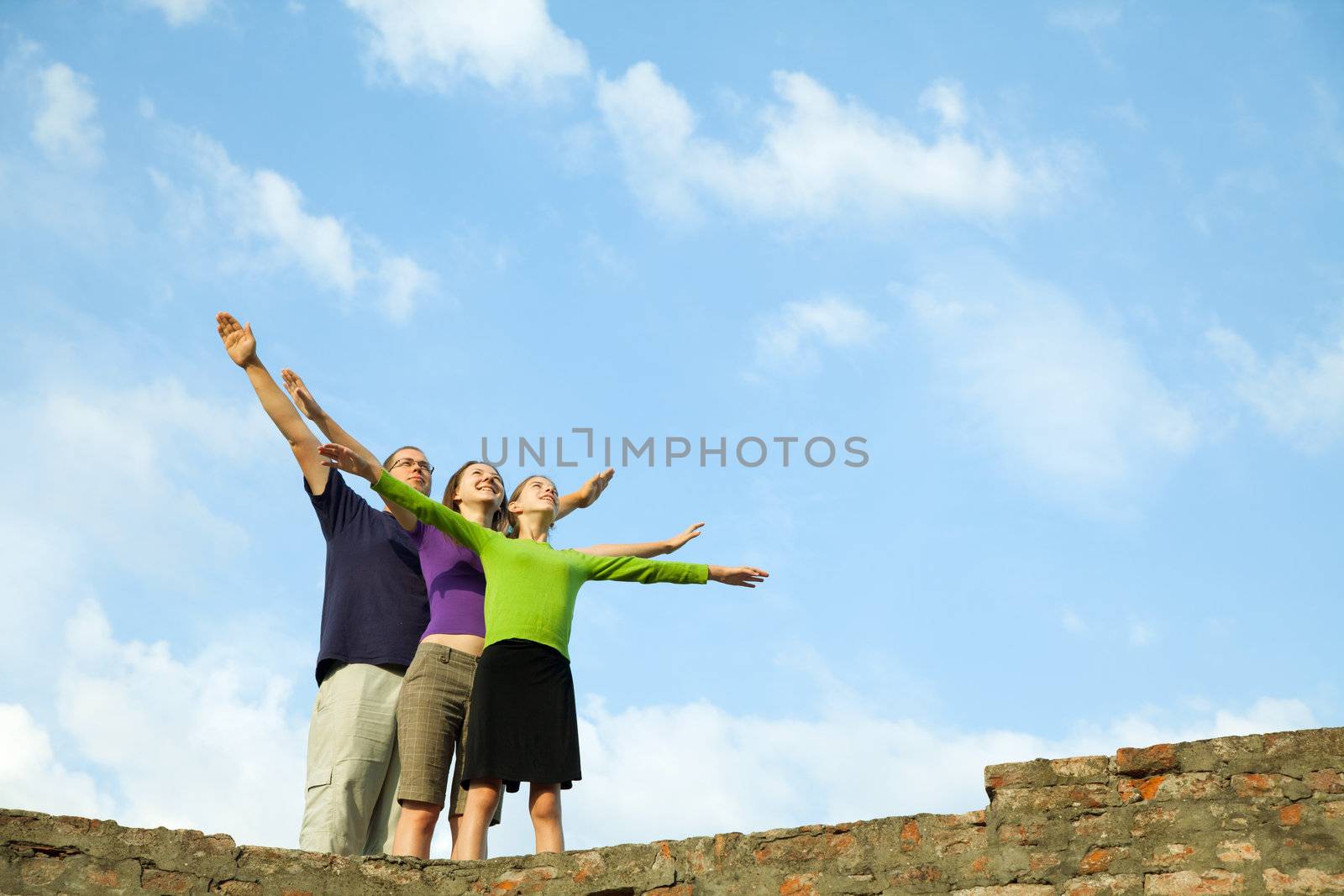 Three young people staying with raised hands against blue sky